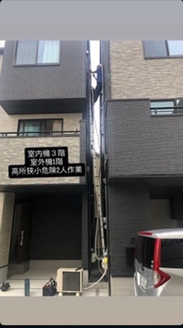 3階建て住宅の狭い隙間にはしごをかけて配管をおろす作業