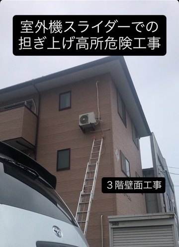 3階建て住宅の外壁にはしごをかけ、室外機を壁面に取り付ける工事